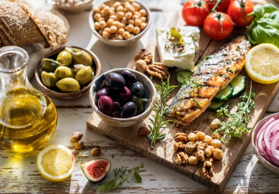 Середземноморські продукти на столі: запечена риба, оливки, оливкова олія, нут, горіхи, овочі, сир, лимон і цільнозерновий хліб