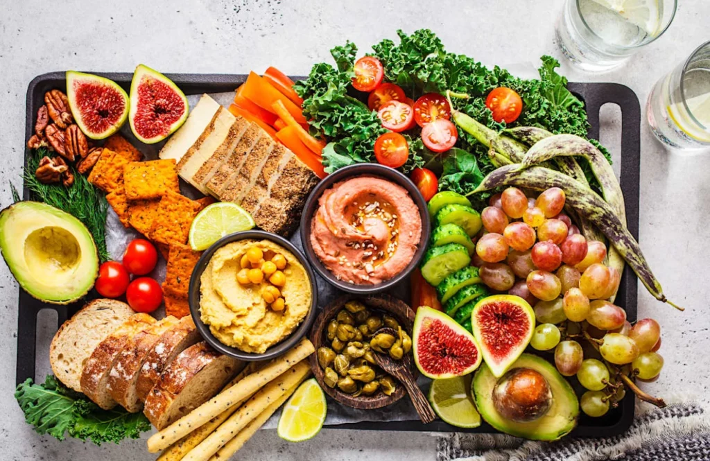 Яскрава тарілка корисних продуктів із хумусом, авокадо, овочами, зеленню, інжиром, виноградом, горіхами та хлібом